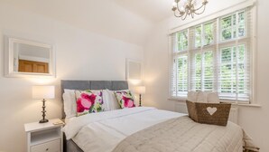 Un dormitorio con cama, mesitas de noche, ventana con persianas y un candelabro.