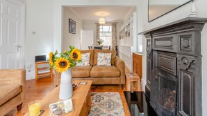 A cozy living room with a brown sofa, a wooden coffee table with a vase of sunflowers, a fireplace, and a bookshelf. - 4 Bed in Swanage (oc-a29454) (Swanage)