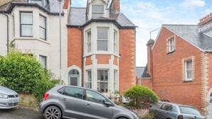 A residential street with two houses, one with a bay window and the other with a traditional design. There are cars parked along the street. - 4 Bed in Swanage (oc-a29454) (Swanage)