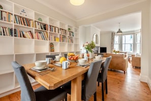 Un coin repas avec une table en bois mise pour le petit-déjeuner, entourée d’étagères remplies de livres.