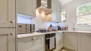 A kitchen with light grey cabinets, a built-in oven, a stove, and a window with a view of greenery. - 4 Bed in Swanage (oc-a29454) (Swanage)