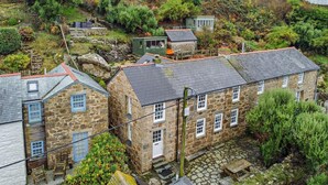 A stone building with multiple windows, a small outdoor seating area, and a surrounding garden. - 3 Bed in Sennen Cove (oc-c29670) (Sennen)