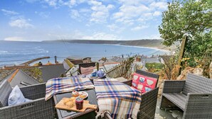A wicker outdoor seating area with a table set for breakfast, overlooking a coastal view. - 3 Bed in Sennen Cove (oc-c29670) (Sennen)