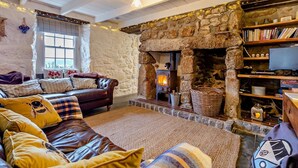 A cozy living room with a stone fireplace, a leather sofa, and a bookshelf. - 3 Bed in Sennen Cove (oc-c29670) (Sennen)
