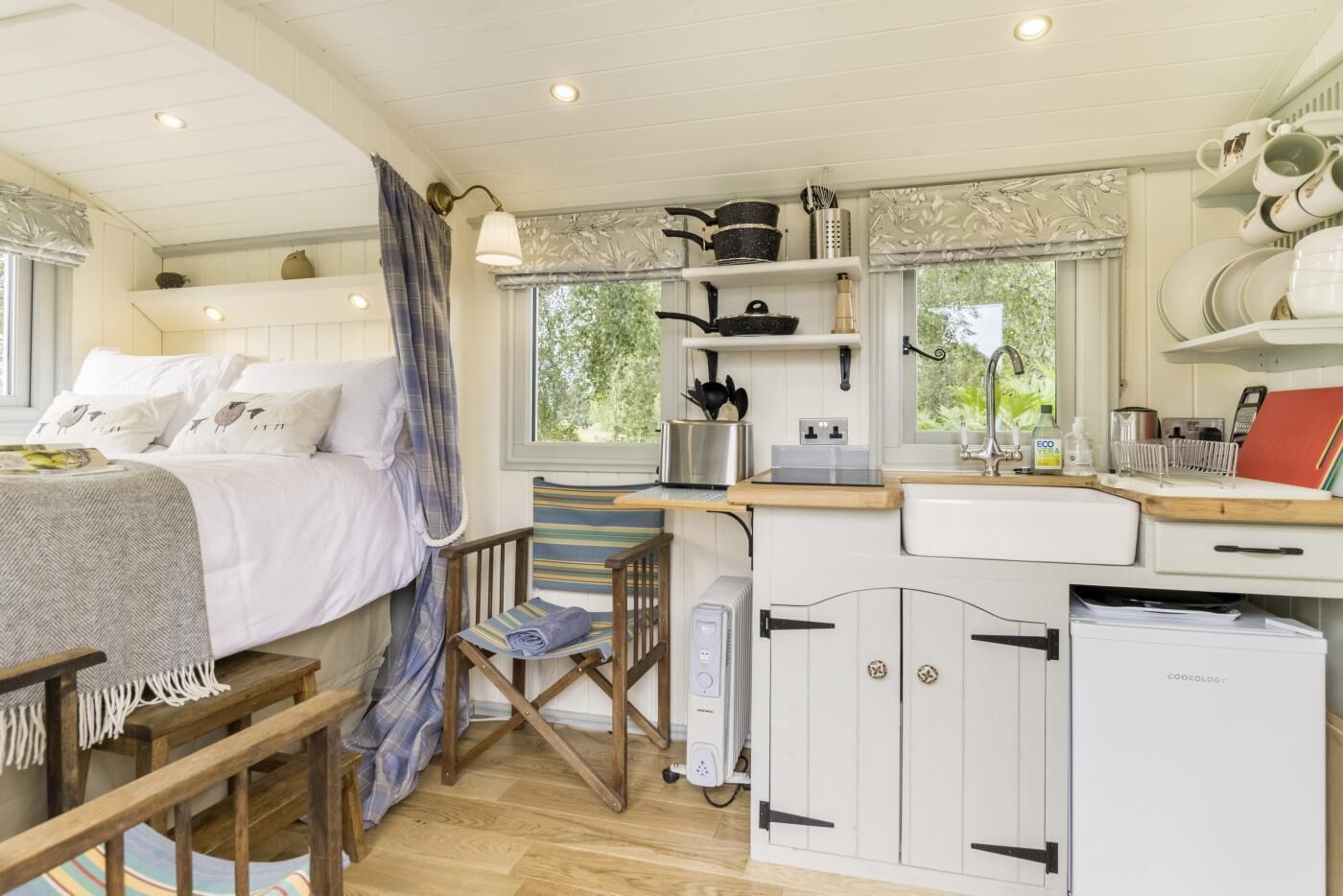 Acogedora habitación estilo cabaña con cama, una silla, una mesita, kitchenette con fregadero y estufa, y ventana con vista a la vegetación.