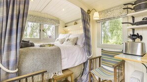 Een knus slaapkamer met een bed, een houten stoel, een klein tafeltje en een raam met gordijnen.