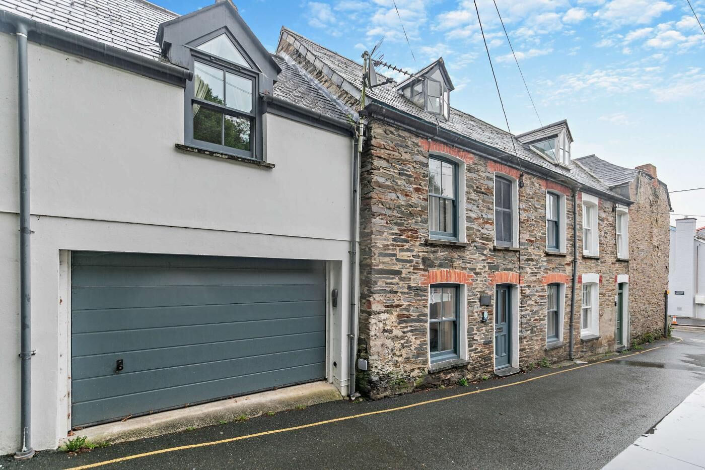 A street view with a grey garage door, a stone building with multiple windows, and a clear sky.