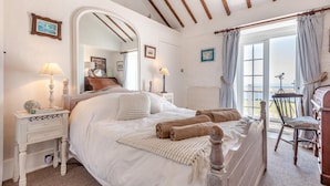 A bedroom with a bed, bedside tables, a mirror, a piano, and a view of the sea. - 2 Bed in Langton Herring (oc-r29848) (Langton Herring)
