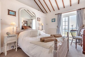 Un dormitorio con cama, mesitas de noche, un espejo, un piano y vista al mar.