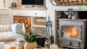 A cozy living room with a fireplace, a television, and a table with pastries and a plant. - 2 Bed in Langton Herring (oc-r29848) (Langton Herring)