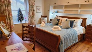Un dormitorio con una cama de madera, un escritorio con una silla, una ventana con cortinas y un pequeño árbol de Navidad.
