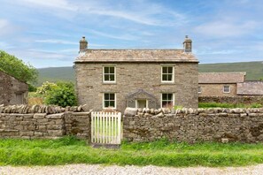 A stone house with a white gate, a small porch, and a stone wall in a rural setting. - 3 Bed in Askrigg (oc-w29833) (Stalling Busk)