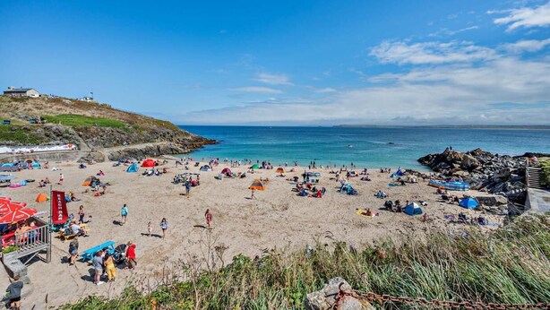 A beach with tents and people, a flag, and a building in the background. - 1 Bed in St. Ives (oc-p29852) (St Ives)