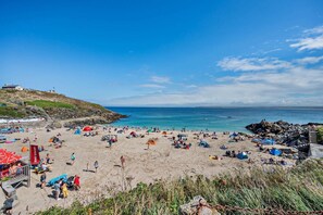 A beach with tents and people, a flag, and a building in the background. - 1 Bed in St. Ives (oc-p29852) (St Ives)