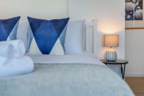 A neatly made bed with pillows, a bedside table with a lamp, and a wall with a painting. - 1 Bed in St. Ives (oc-p29852) (St Ives)