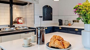 A modern kitchen with white countertops, a black stove, a coffee maker, and a vase with flowers.