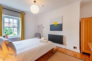 Une chambre à coucher avec un lit, un radiateur, une fenêtre avec des rideaux et un tableau accroché au mur.
