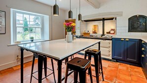 A modern kitchen with a central island, pendant lights, and a view of the outdoors through a large window.