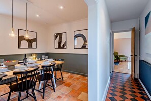 Un espace repas avec une table dressée pour quatre personnes, des chaises et des lampes suspendues.