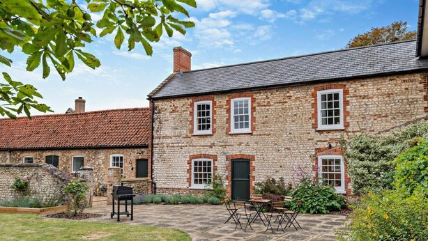 A stone house with a tiled roof, a paved courtyard, and outdoor seating.