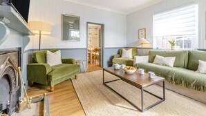 Ein Wohnzimmer mit Kamin, zwei grüne Sofas, einem Couchtisch und einem Essbereich.