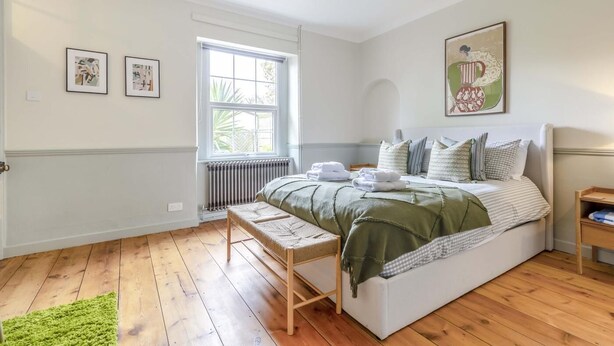 Ein Schlafzimmer mit einem großen Bett, einem Fenster, einem Heizkörper und Kunstwerken an den Wänden.