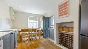 Eine moderne Küche mit Holzboden, einer Essecke mit Stühlen, einer eingebauten Weinstauraum und einem Kühlschrank.