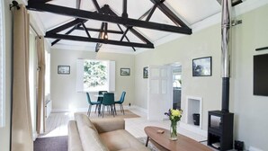 A modern living room with a sofa, a wooden coffee table, a fireplace, and a dining area with chairs. - 1 Bed in Northrepps (oc-m29800) (Crossdale Street)