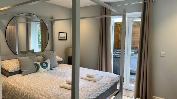 A four-poster bed with a patterned bedspread, a round mirror above it, and a view of a balcony through a glass door. - 1 Bed in Northrepps (oc-m29800) (Crossdale Street)