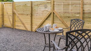 A patio area with a round metal table, two chairs, and a wooden fence. - 1 Bed in Tebay (oc-m29886) (Mount Pleasant)
