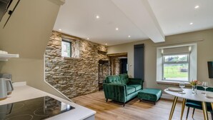 A modern kitchen with a stone accent wall, a green sofa, and a dining area with a table and chairs. - 1 Bed in Tebay (oc-m29886) (Mount Pleasant)
