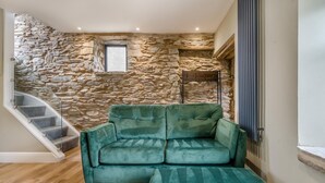 A room with a stone wall, a green sofa, a wooden floor, and a staircase. - 1 Bed in Tebay (oc-m29886) (Mount Pleasant)