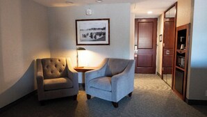 A hotel room with two armchairs, a small table with a lamp, a framed picture on the wall, and a wooden door. - Executive King Room with with Modern Amenities & Breakfast (Hillsdale)