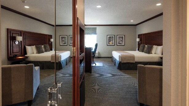 A hotel room with two beds, a desk, and a chair. There are framed pictures on the wall and a window with a view. - Executive King Room with with Modern Amenities & Breakfast (Hillsdale)