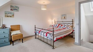 Une chambre à coucher avec un lit en métal, une commode bleue, une chaise en osier et un luminaire au plafond.