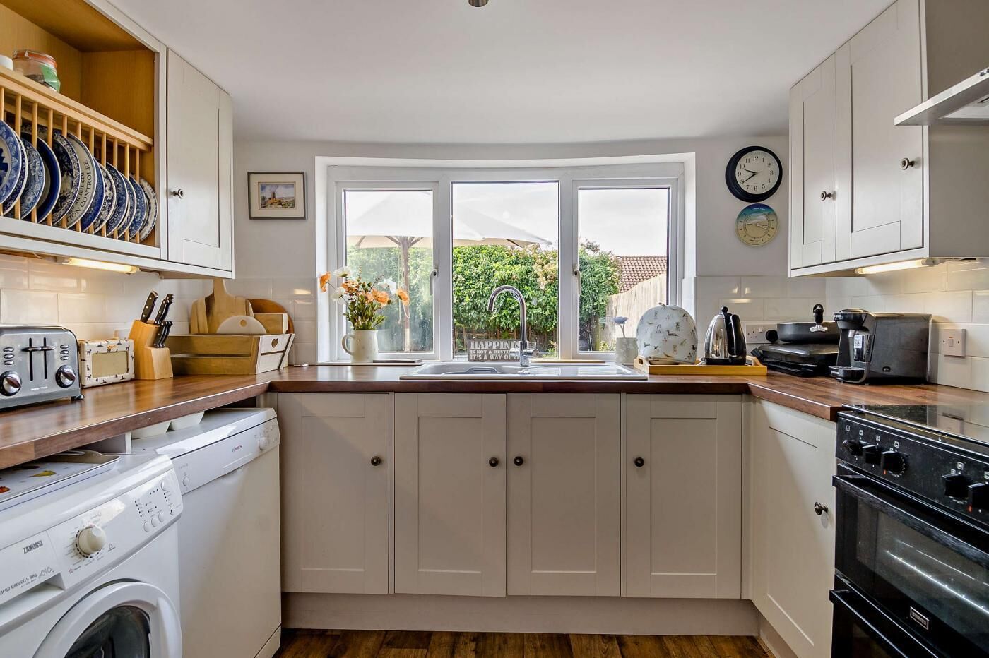 A kitchen with white cabinets, a wooden countertop, a washing machine, a stove, and a window with a view of greenery.