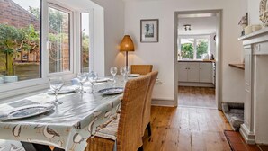 Un coin repas avec une table dressée pour six personnes, une chaise en osier et une lampe.