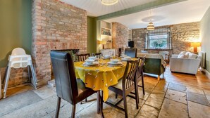 A dining area with a brick wall, a table set for four, and a view of the kitchen and living area. - 3 Bed in Swanage (oc-n29755) (Swanage)