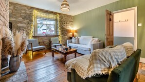 A cozy living room with a stone wall, a wooden coffee table, a sofa, and a chair. - 3 Bed in Swanage (oc-n29755) (Swanage)