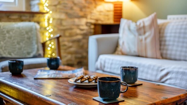 A cozy living room with a wooden coffee table, two mugs, a plate of cookies, and a lamp. - 3 Bed in Swanage (oc-n29755) (Swanage)