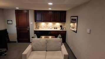 A compact living space with a kitchenette, a sofa, and a door leading to another room.