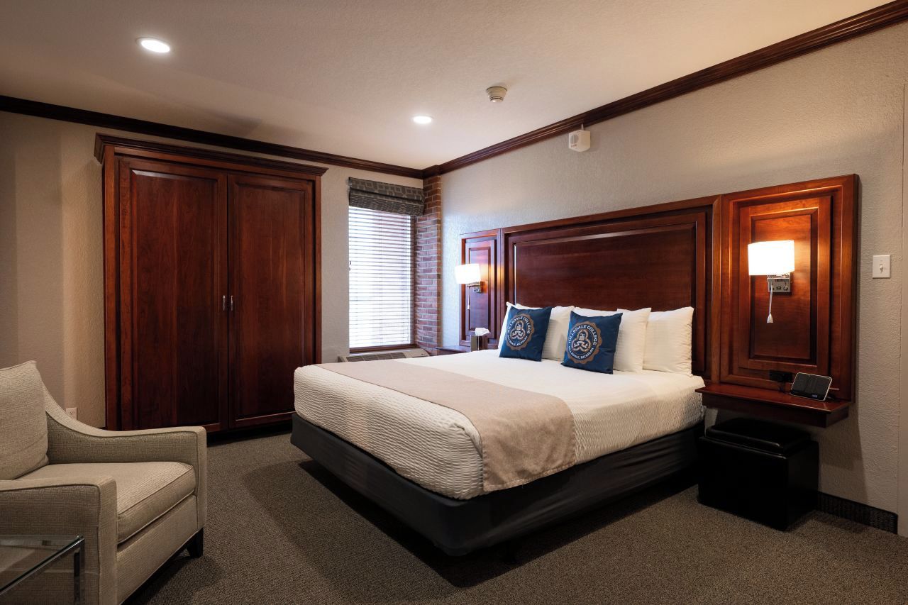 A hotel room with a large bed, a chair, a desk, and a wardrobe.