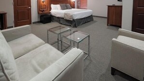 Een hotelkamer met een bed, twee fauteuils, een glazen bijzettafeltje, een bureau en een kledingkast.