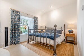 Une chambre à coucher avec un lit en métal, une fenêtre avec des rideaux, une table de chevet avec une lampe et un radiateur.