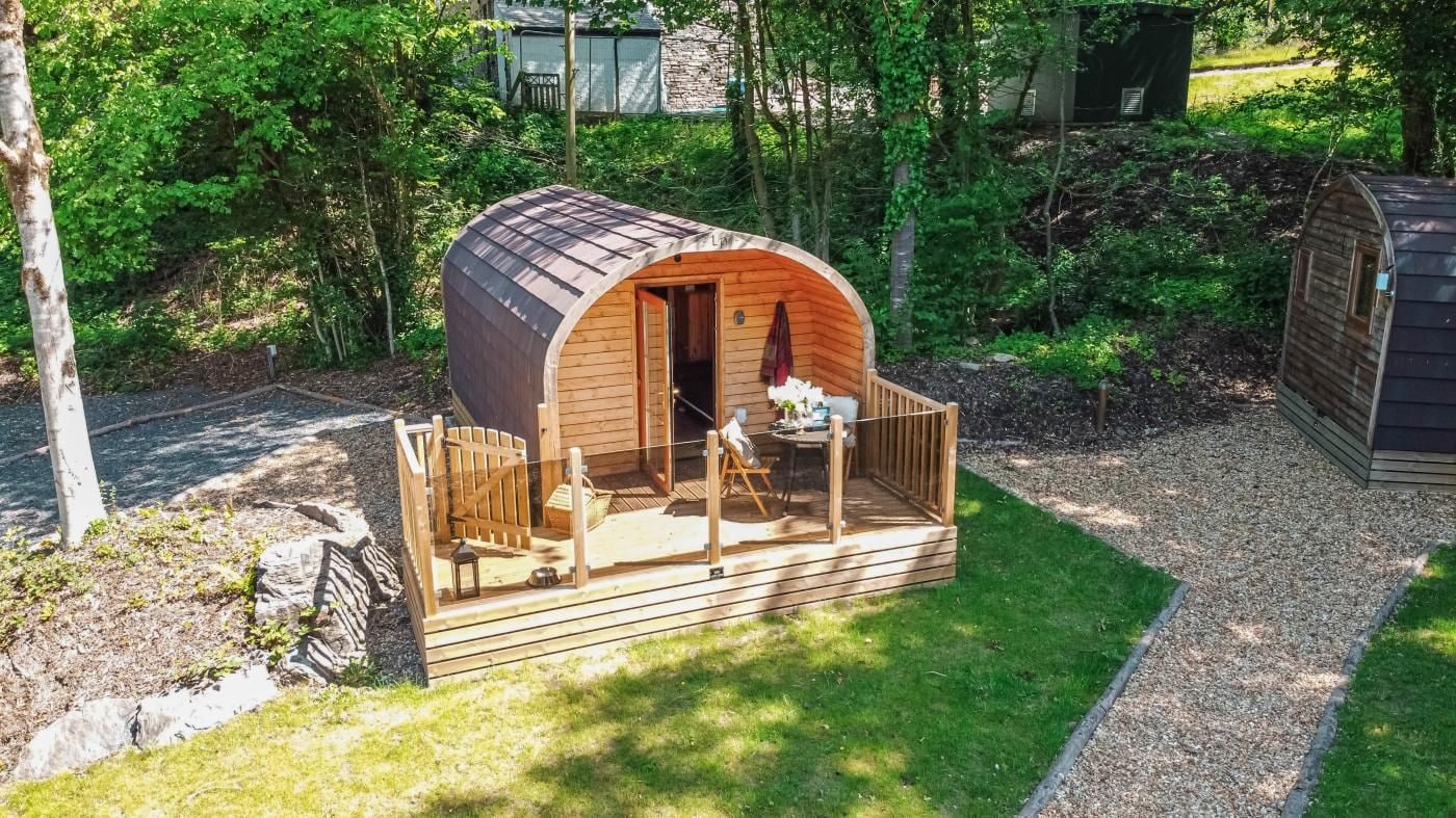 A small wooden cabin with a curved roof, a deck, and a table and chairs outside.
