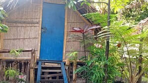 A bamboo structure with a blue door, surrounded by dense foliage.
