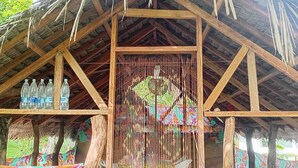 A rustic wooden structure with a thatched roof, featuring a colorful mural and a woven basket hanging from the ceiling.