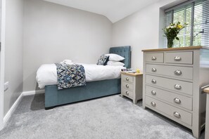 A bedroom with a bed, bedside table, dresser, and a window with blinds. - 3 Bed in Newby Bridge (oc-c29820) (Newby Bridge)