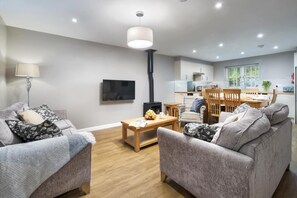 A modern living room with a sofa set, a coffee table, and a television. There is a kitchen area with a dining table and chairs.