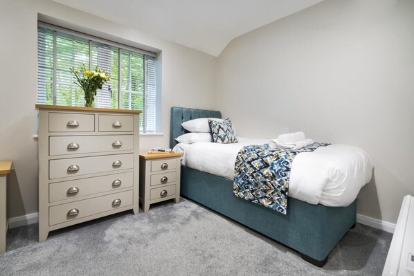 A bedroom with a bed, a dresser, a nightstand, and a window with blinds.